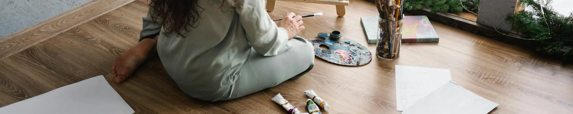 woman sitting, painting on hardwood flooring and looking out at the ocean